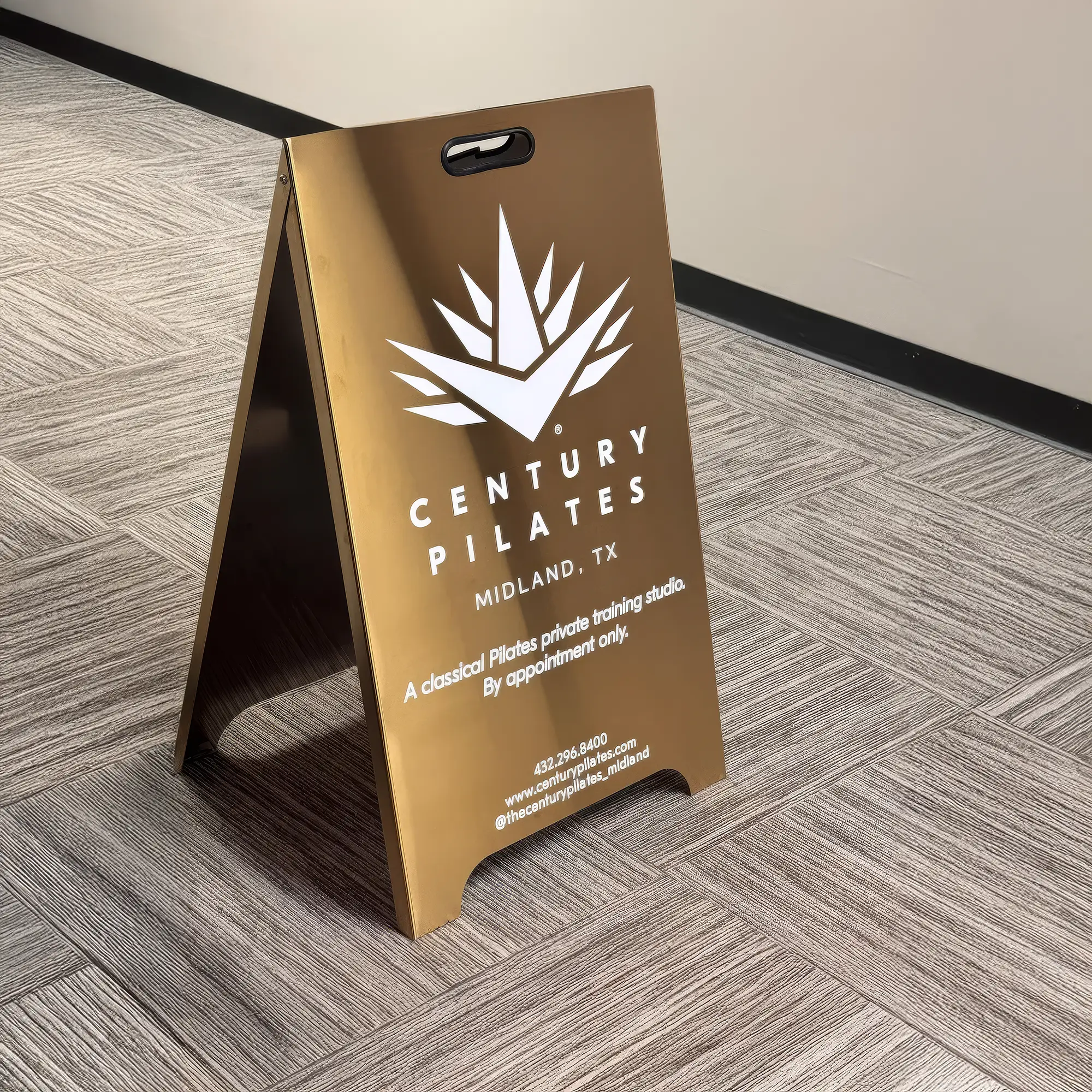 Custom brushed brass A-frame sign displaying white branding and studio information for 'Century Pilates'.